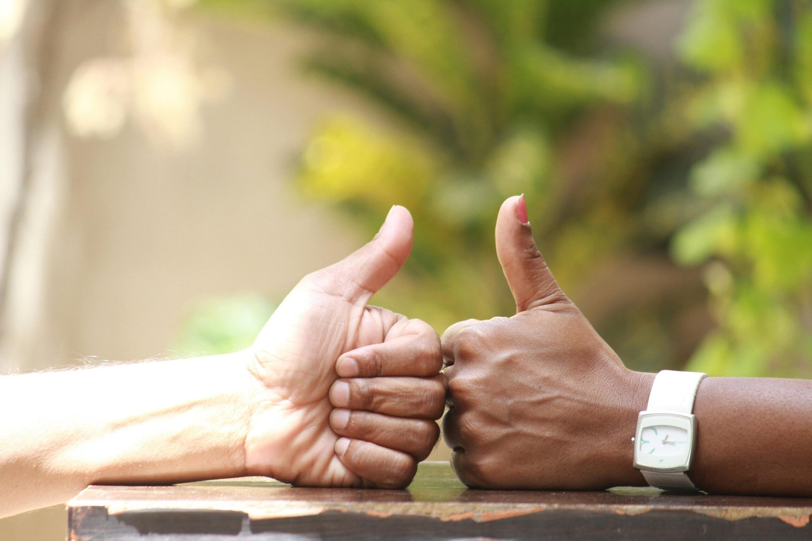 Close-up of two people giving thumbs up outdoors, symbolizing agreement.